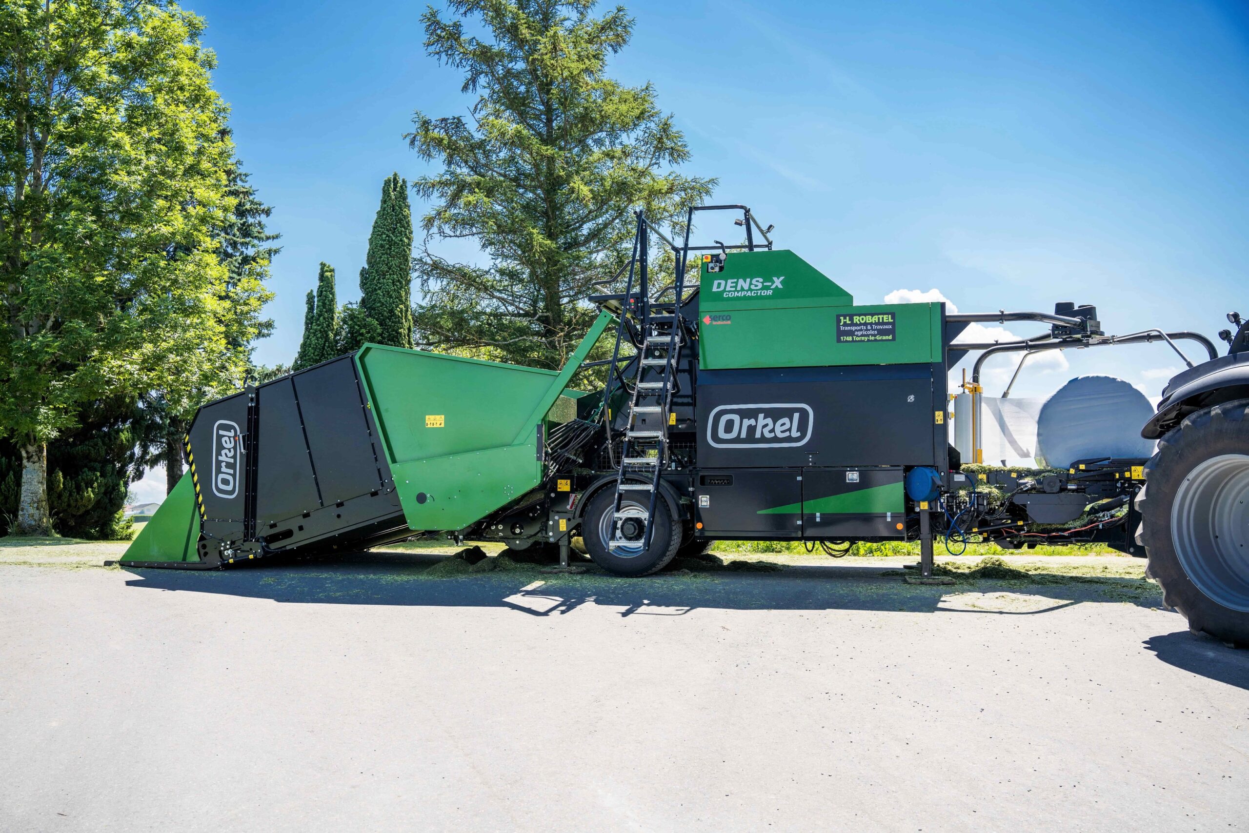 Side shot of a Dens-X on a concrete ground with two green trees and a blue sky in the background.