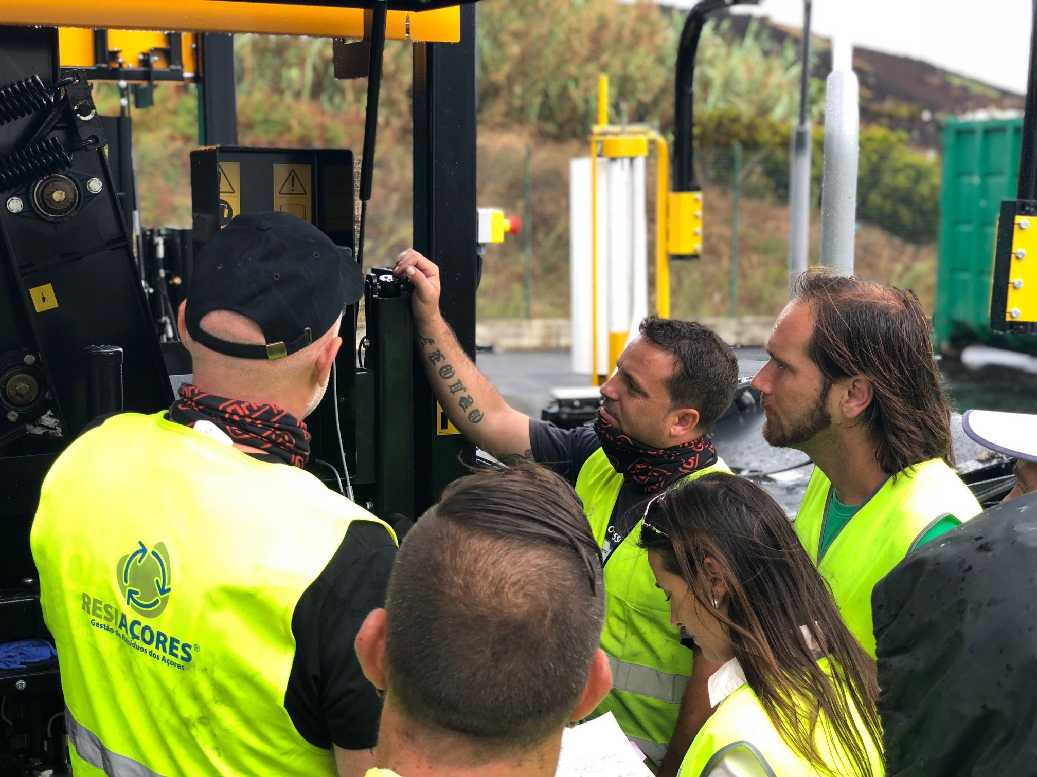 Techniker in gelben Sicherheitswesten versammelten sich vor einer schwarz-gelben Maschine.