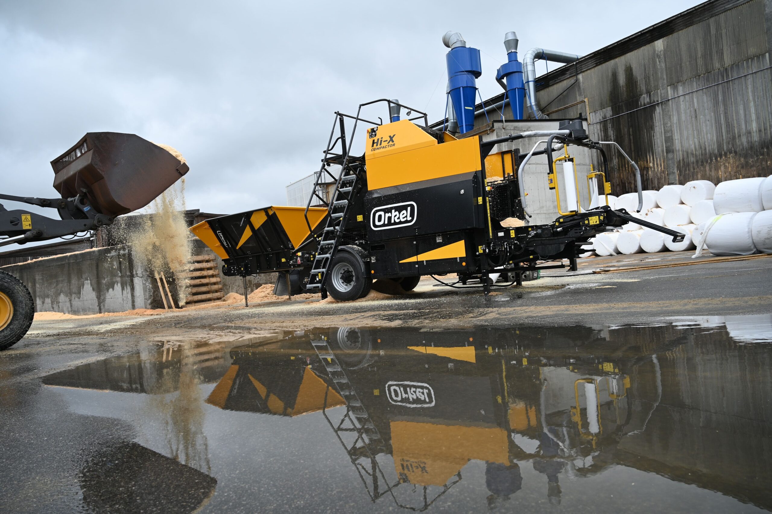 A Hi-X compactor on a concrete flooring, with water pooling in front of it reflecting the machine as an upside-down image.