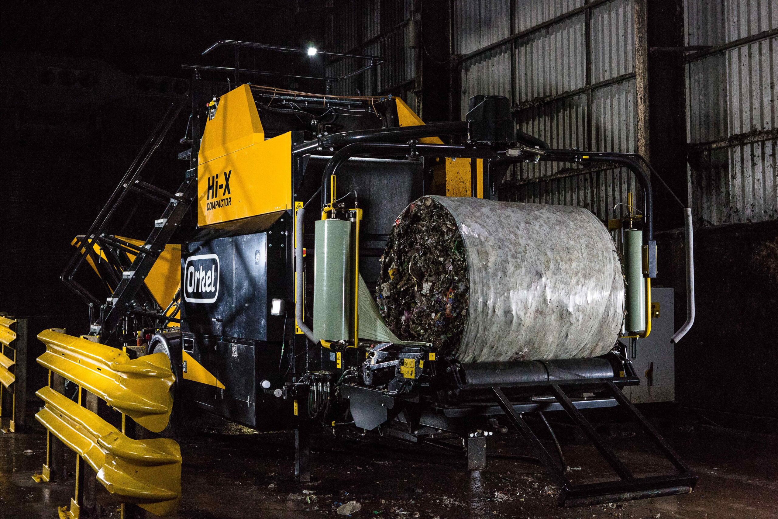 A Hi-X compactor with a half-wrapped waste bale on its wrapping table.