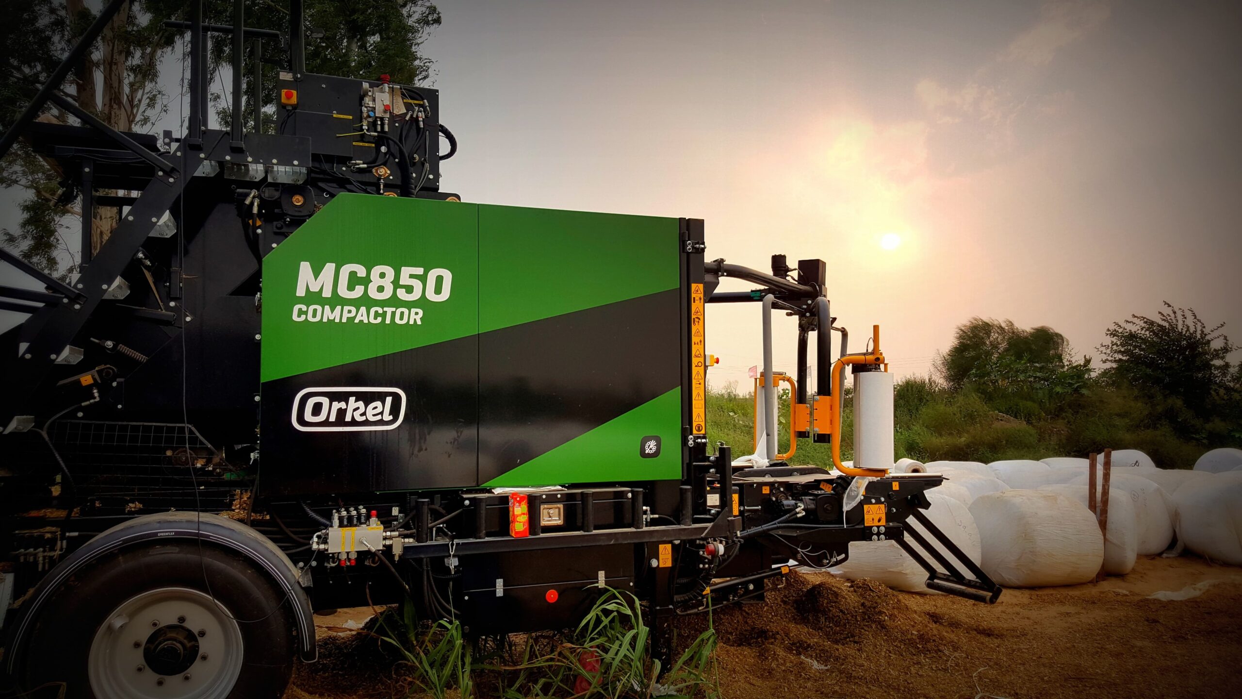 An MP850 compactor in a field during sunset, with round bales in the background.