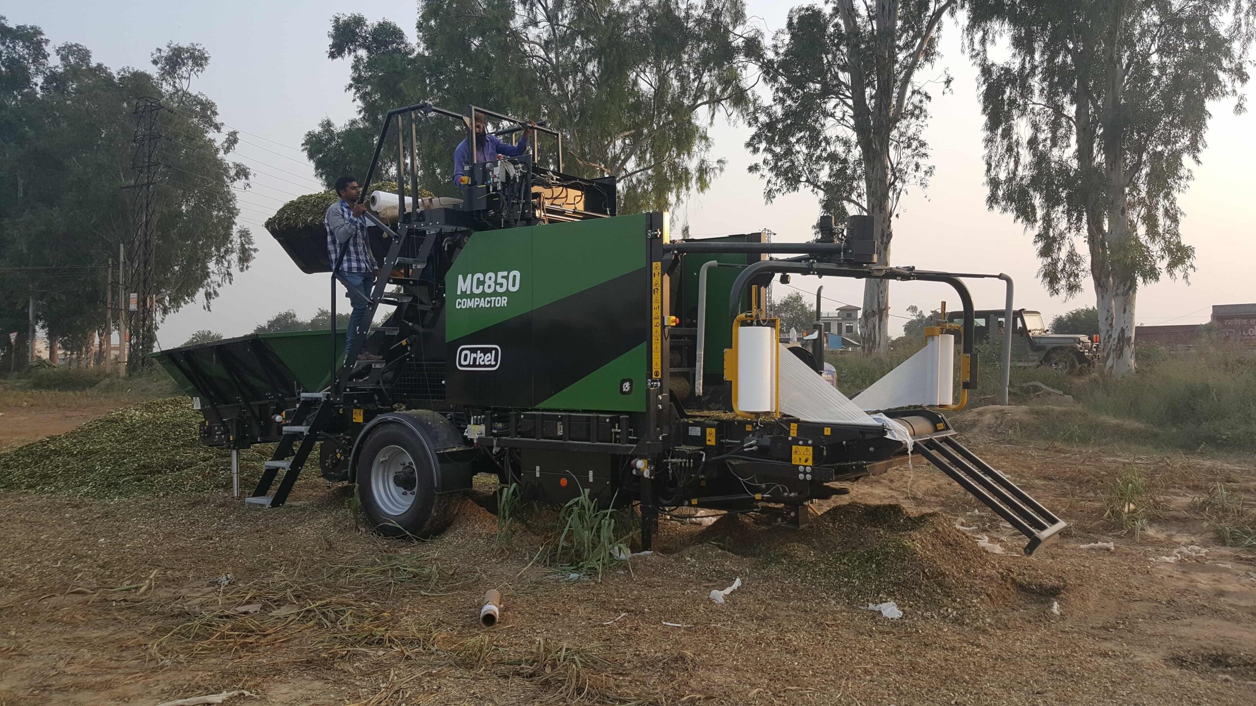 An MP850 compactor in a field, with brown grass flooring and trees in the background..