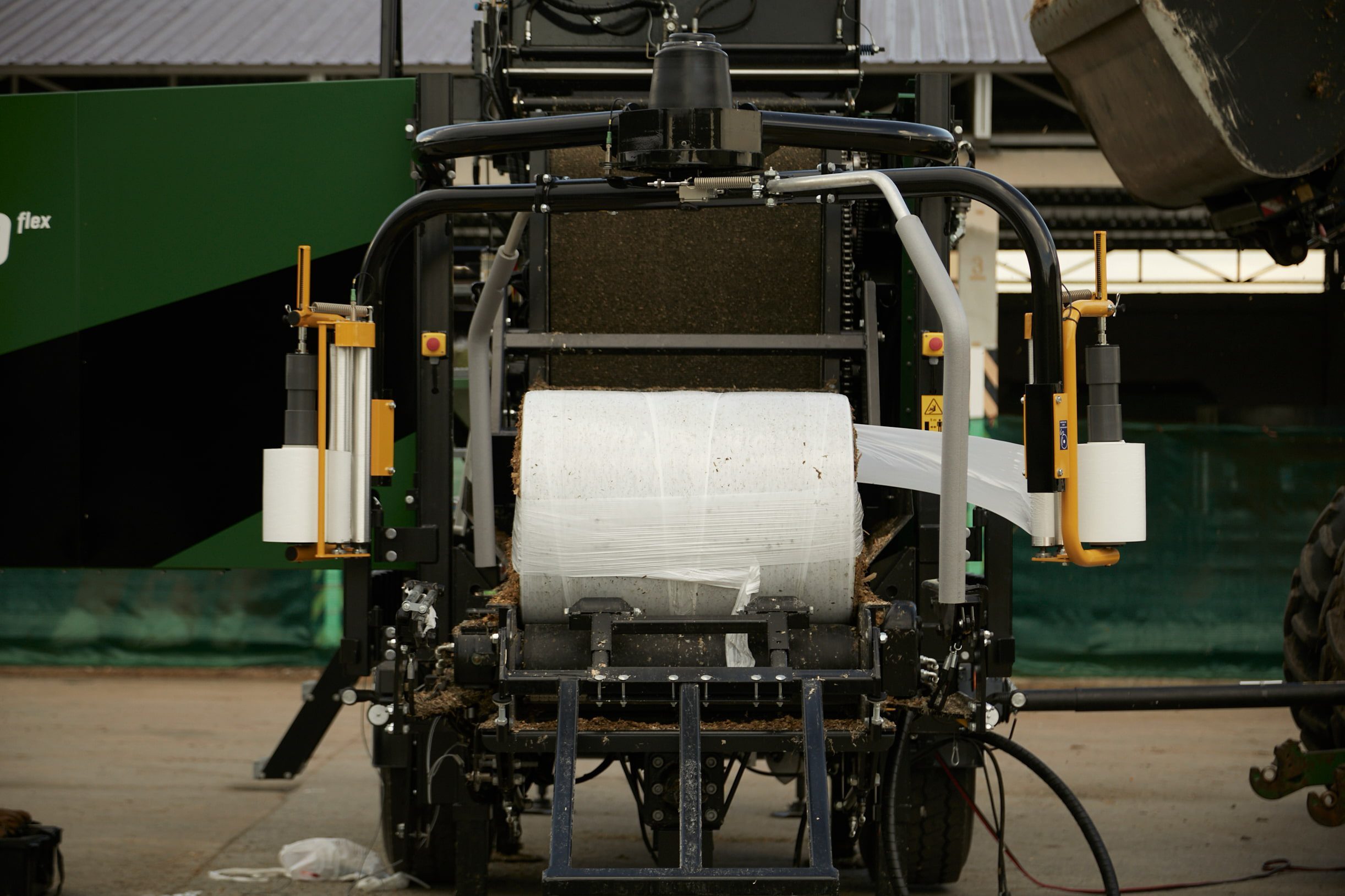 A half-wrapped bale with brown grassy material on a wrapping table.