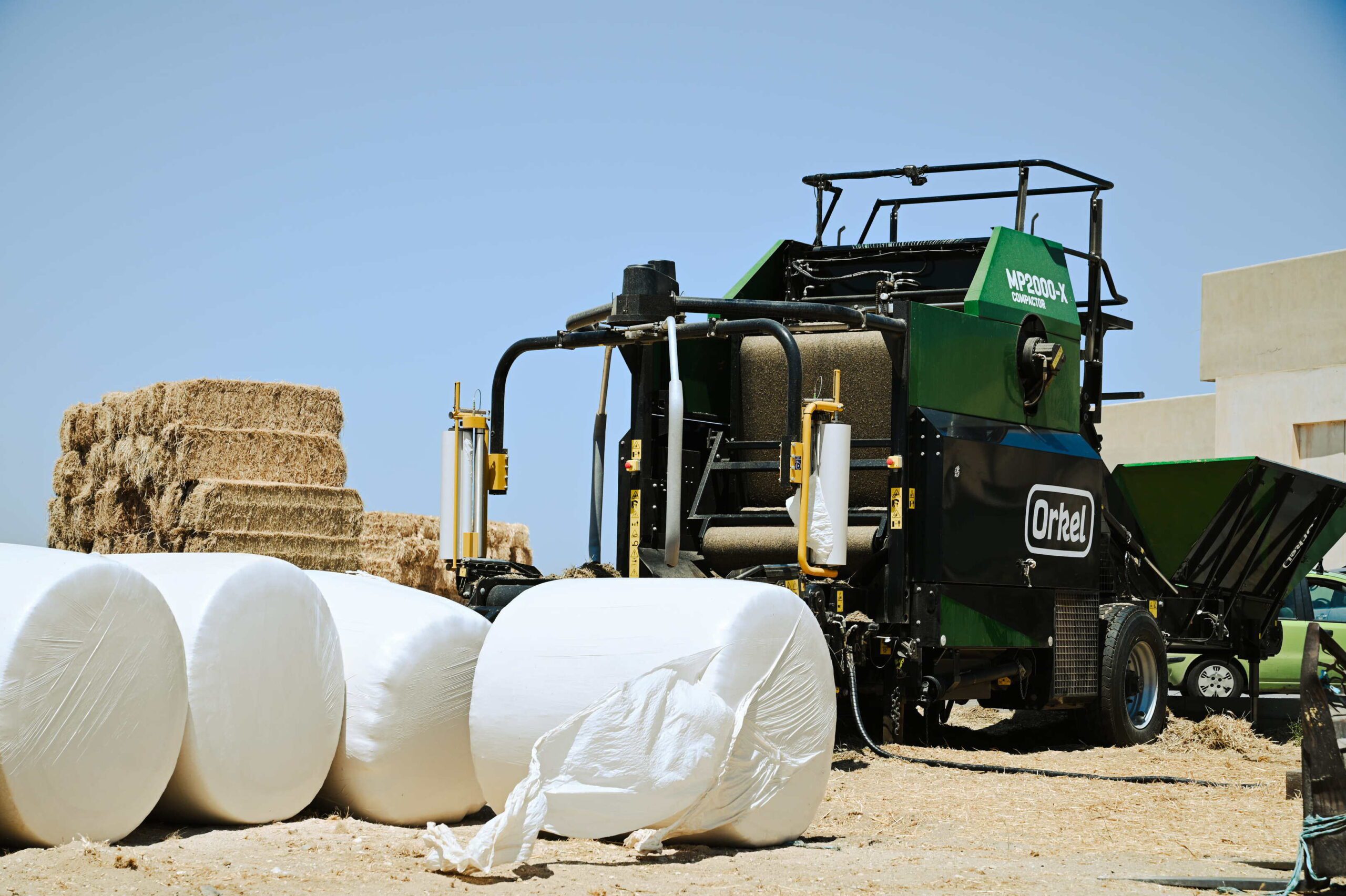 An MP2000-X behind four newly wrapped round bales lying on their curved side.
