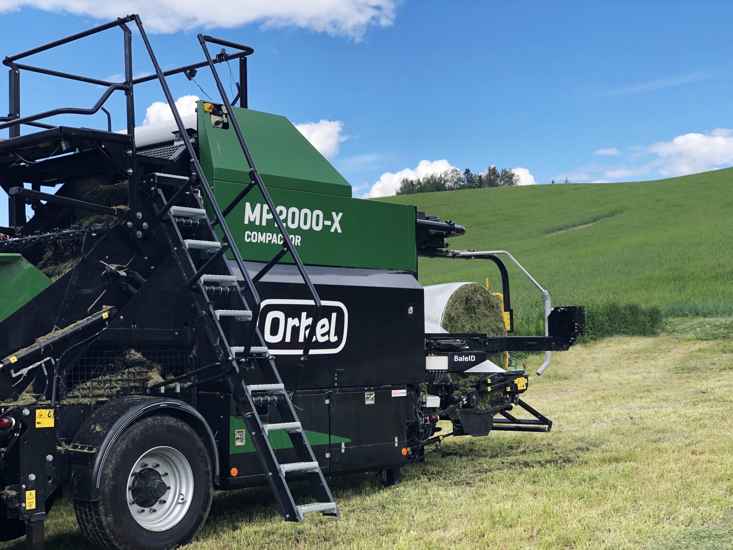 An MP2000-X compactor in a green field with the stairs and the chamber facing the camera.