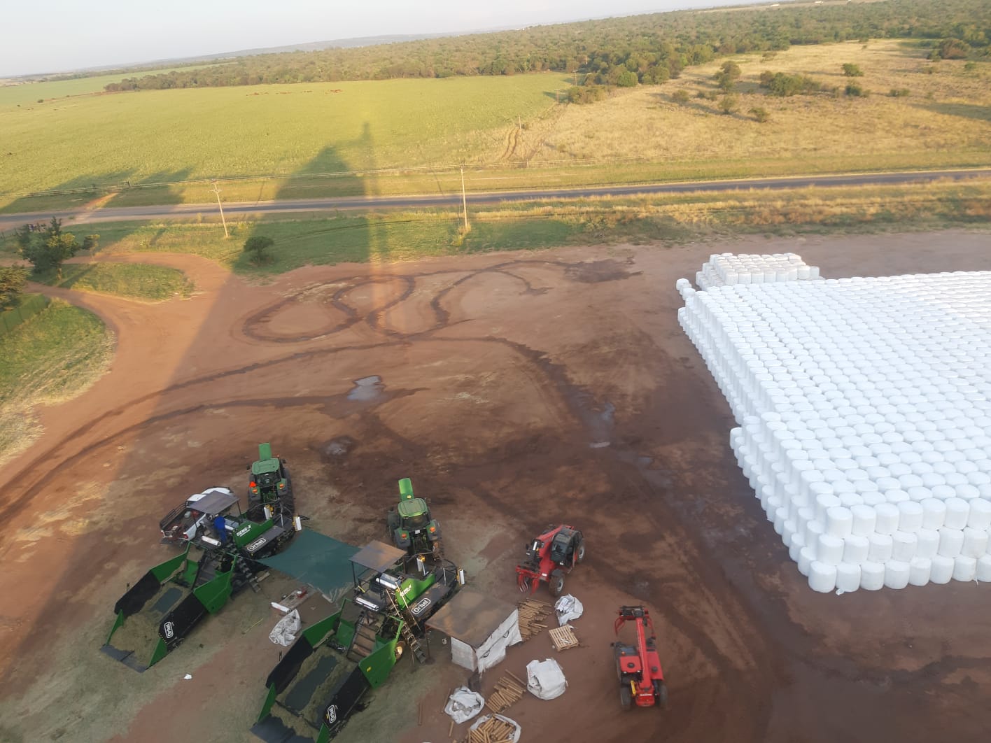 Two Orkel compactors seen from above on a big field, with a huge stack of white round bales to the right