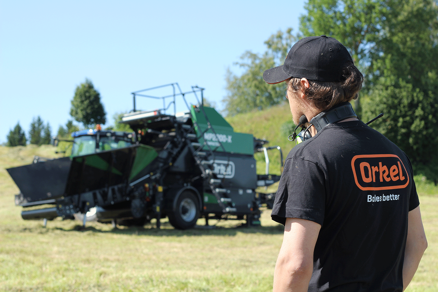 A man in the foreground and a Orkel compactor in the background on a green field giving customer service