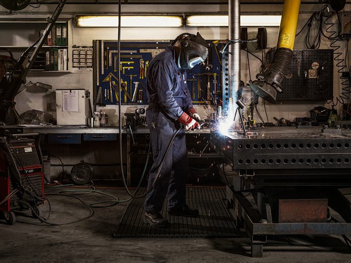Unsere Geschichte: Mann in Schutzkleidung schweißt Metall