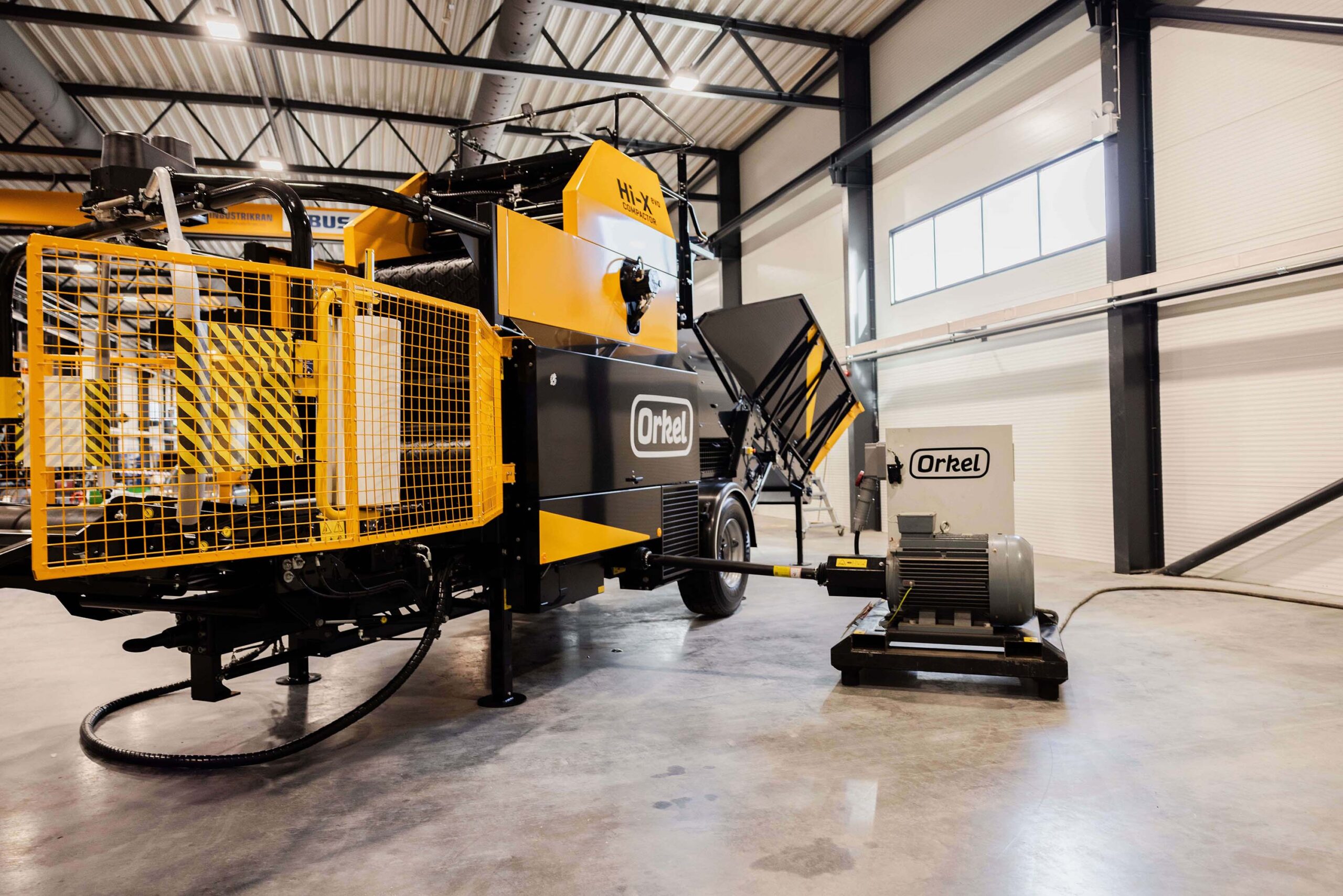 Yellow Orkel compactor in a factory building with an electric powerpack by its side