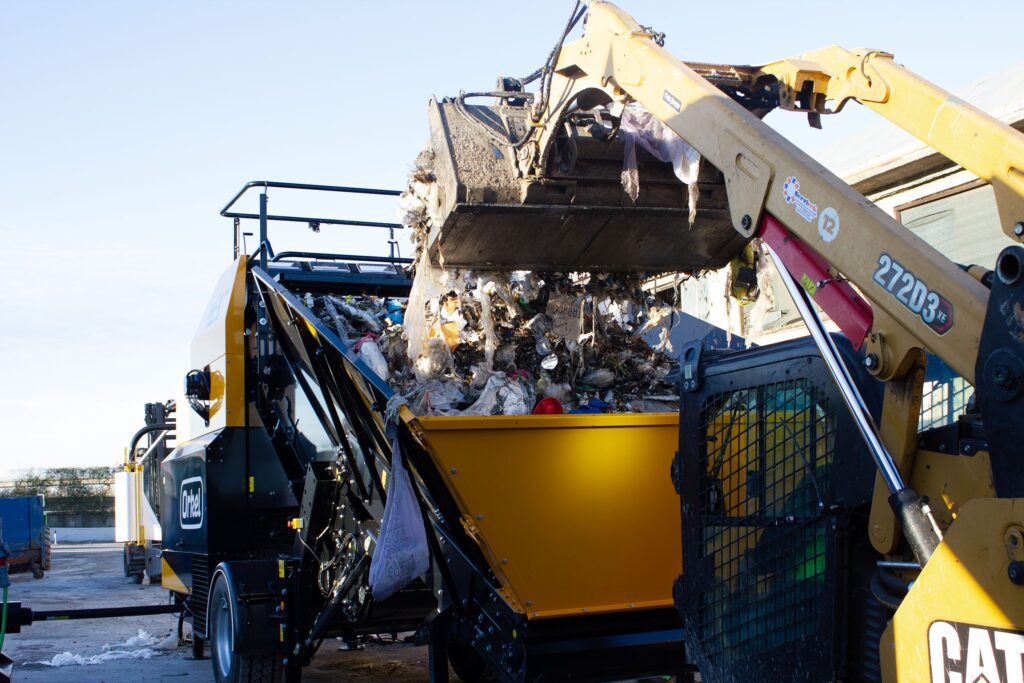 Ein Frontlader entleert Abfall in den Aufnahmetrichter eines Orkel-Kompaktors.