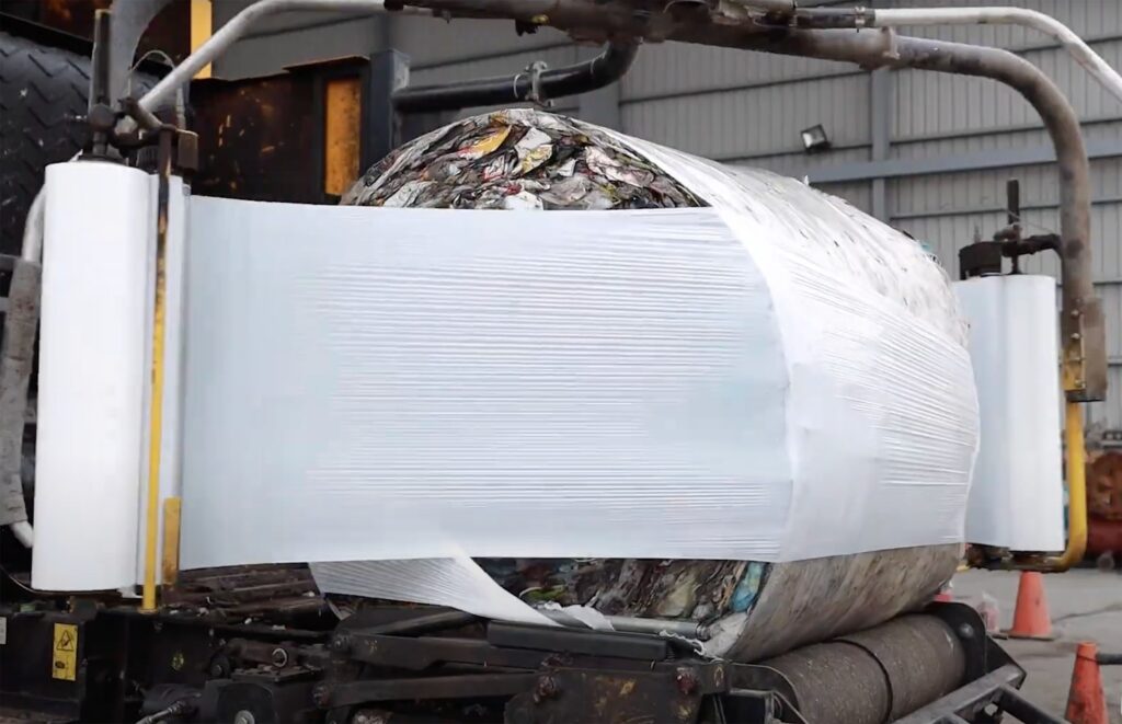 Gros plan sur une balle ronde de déchets broyés en cours d'enrubannage plastique avec un compacteur industriel